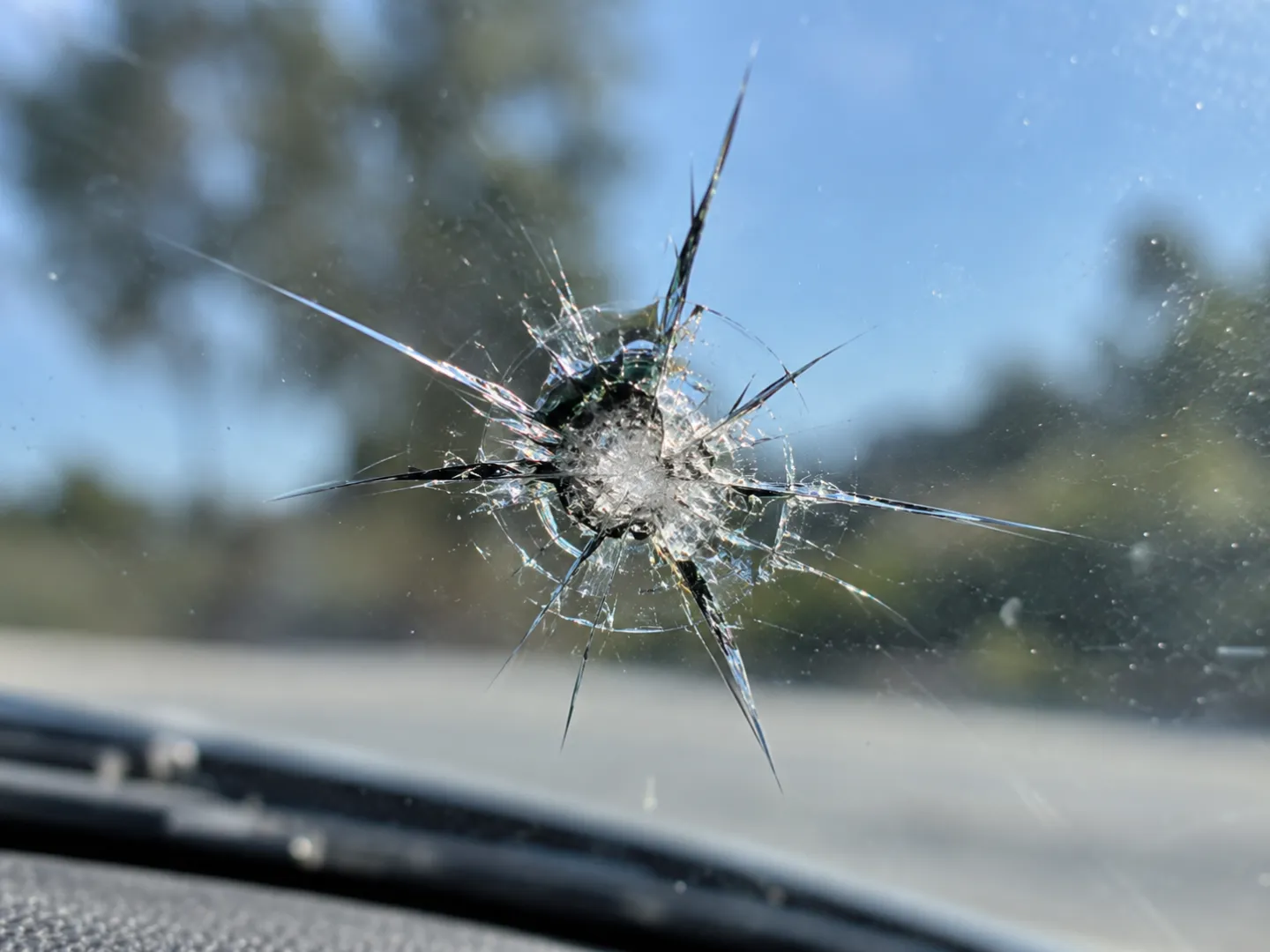 Starburst crack in windshield glass, daylight close-up